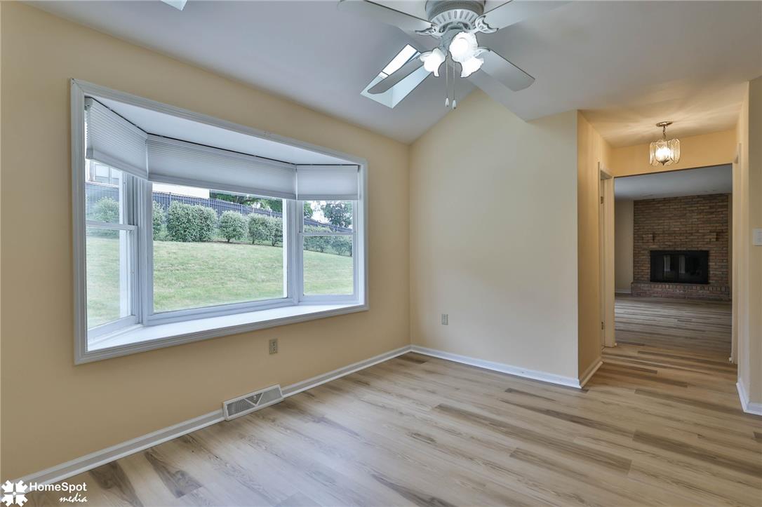 4059 Wedgewood Road Allentown, PA 18104 - Photo 12 of 72 Sun-filled room boasts a bay window and durable plank flooring, offering a cozy retreat with a peek into a brick fireplace beyond.