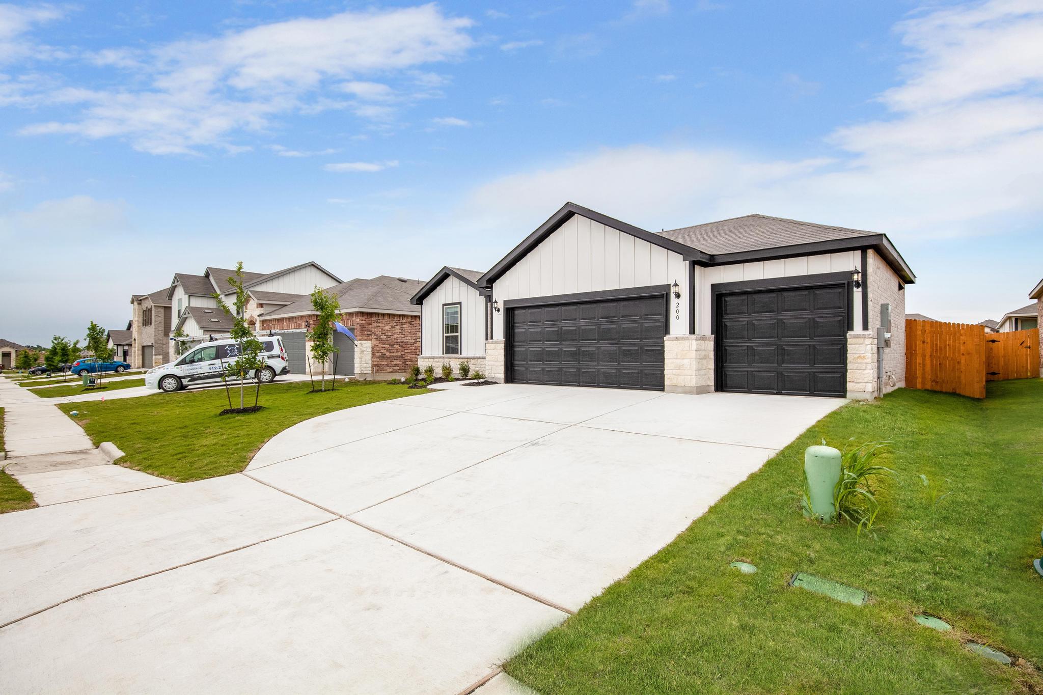 A striking modern residence boasts a multi-car garage with bold dark doors and a neatly manicured lawn.