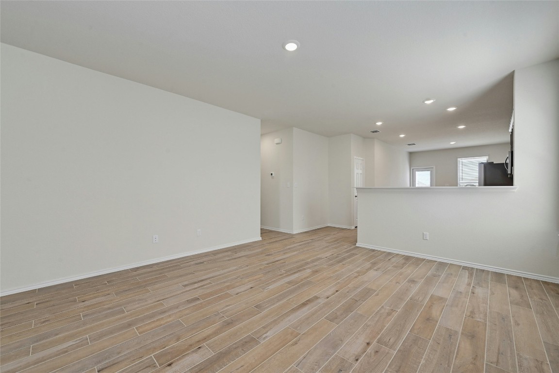 529 Tree Nut Loop Buda, TX 78610 - Photo 8 of 37 an empty room with wooden floor and kitchen view