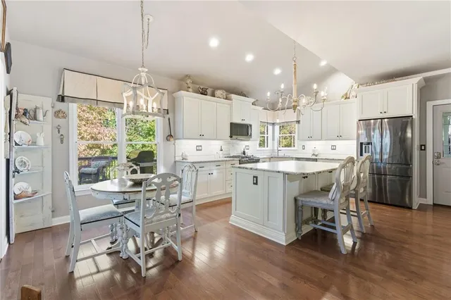 a kitchen with stainless steel appliances kitchen island granite countertop a refrigerator a stove a dining table and chairs with wooden floor