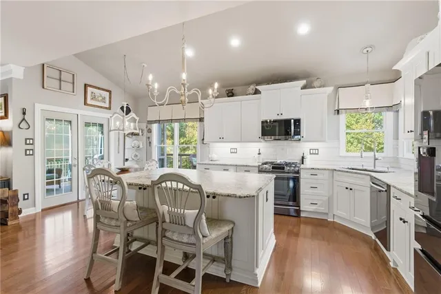 a kitchen with stainless steel appliances granite countertop a stove top oven a sink dishwasher a dining table and chairs with wooden floor