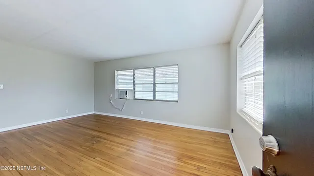 a view of an empty room with wooden floor and a window