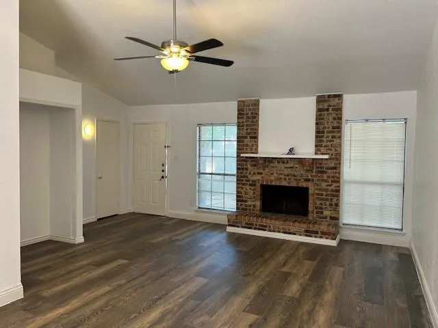 a view of a livingroom with a fireplace a ceiling fan and windows