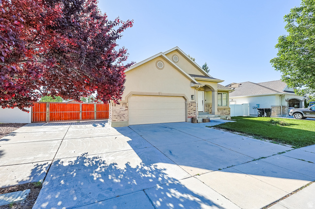 5525 Hampton Way Stansbury Park, UT 84074 - Photo 2 of 35 Exterior showcasing a neutral stucco finish with stone accents, a two-car garage, and a concrete driveway