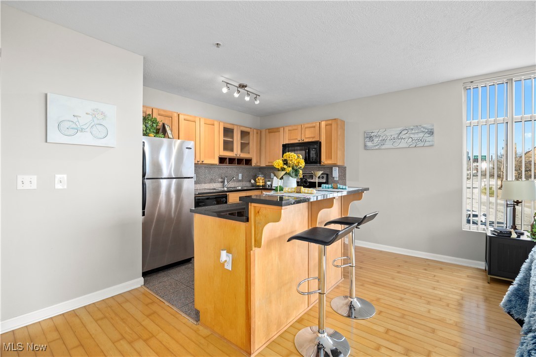 2222 Detroit Avenue, Unit 519 Cleveland, OH 44113 - Photo 7 of 30 Kitchen featuring light hardwood flooring, a kitchen bar, tasteful backsplash, freestanding refrigerator, and black microwave