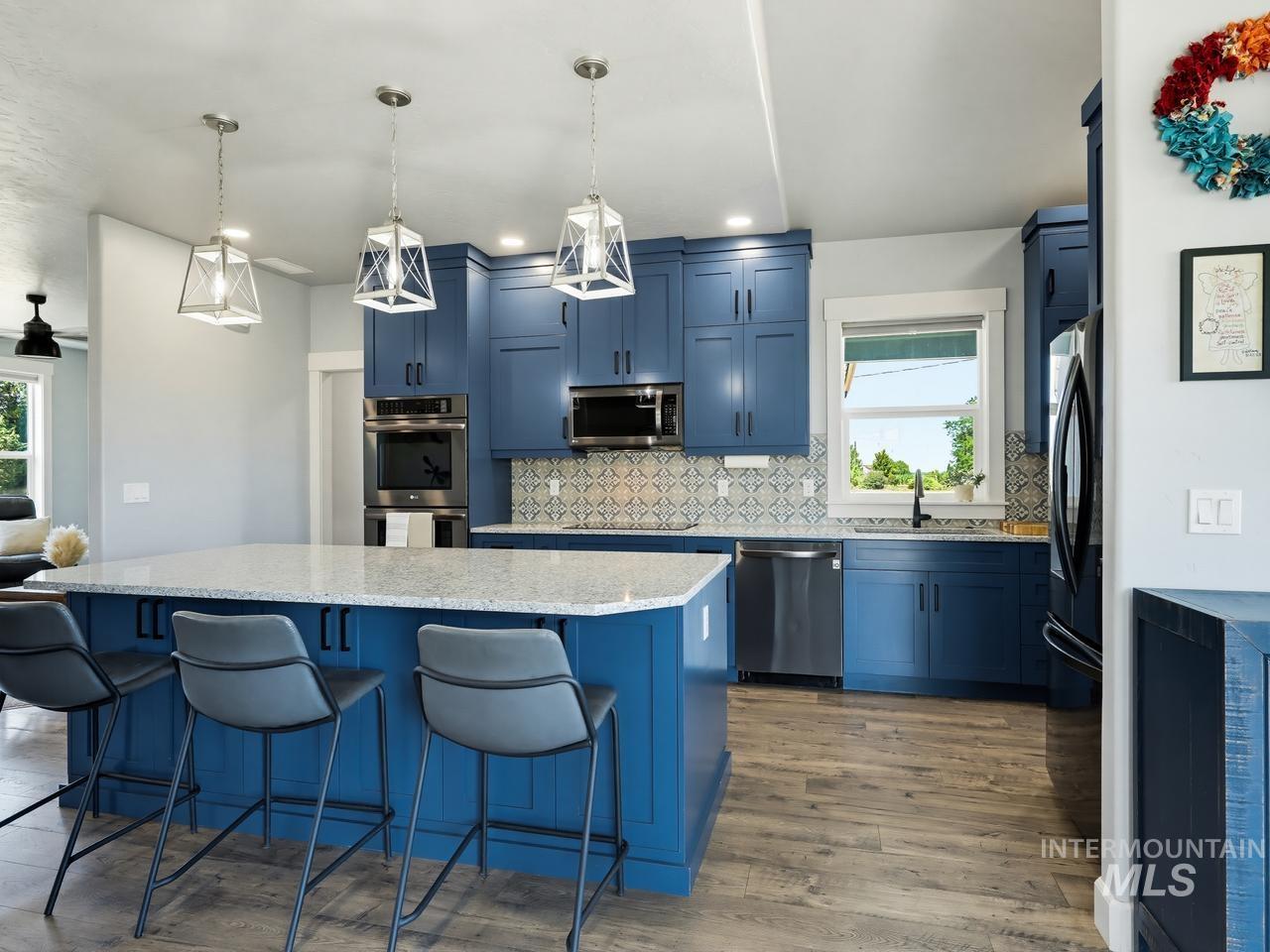 4950 West Columbia Road Nampa, ID 83687 - Photo 13 of 50 Kitchen featuring an expansive island with seating, blue cabinetry, stainless steel appliances, patterned tile backsplash, and wood-finish flooring