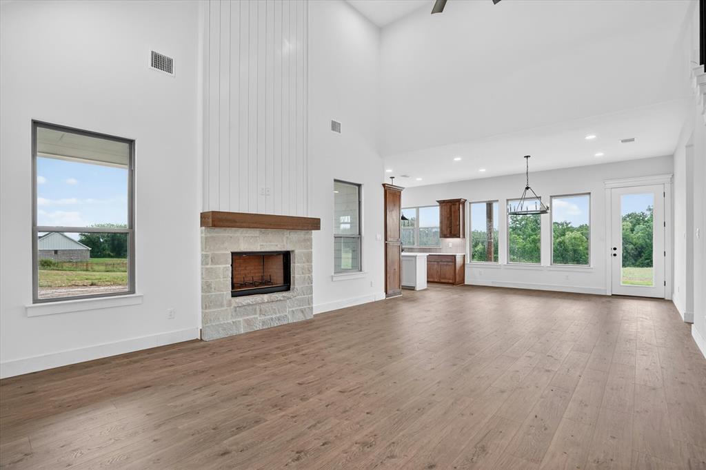 225 Kilkenny Road Poolville, TX 76487 - Photo 5 of 36 Spacious interior featuring a stone-faced fireplace with wood mantel, vaulted ceilings, and wood-finish flooring