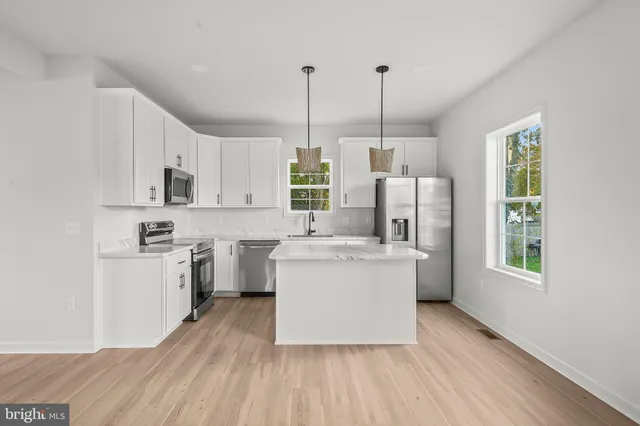 a kitchen with stainless steel appliances a stove a sink dishwasher a refrigerator and white cabinets with wooden floor