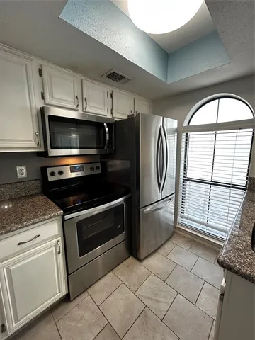 a kitchen with granite countertop a stove a microwave a refrigerator and cabinets