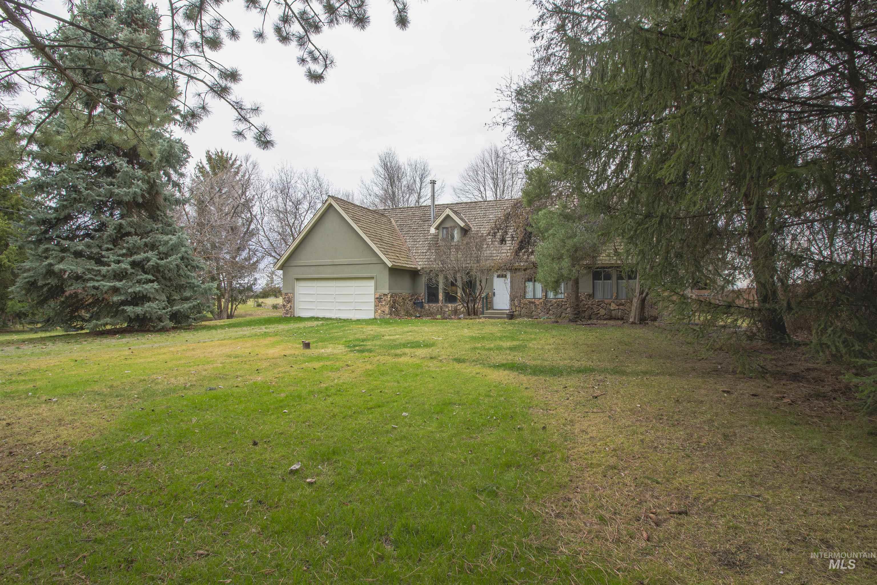 Front of house featuring stone siding, an attached garage, and a front lawn