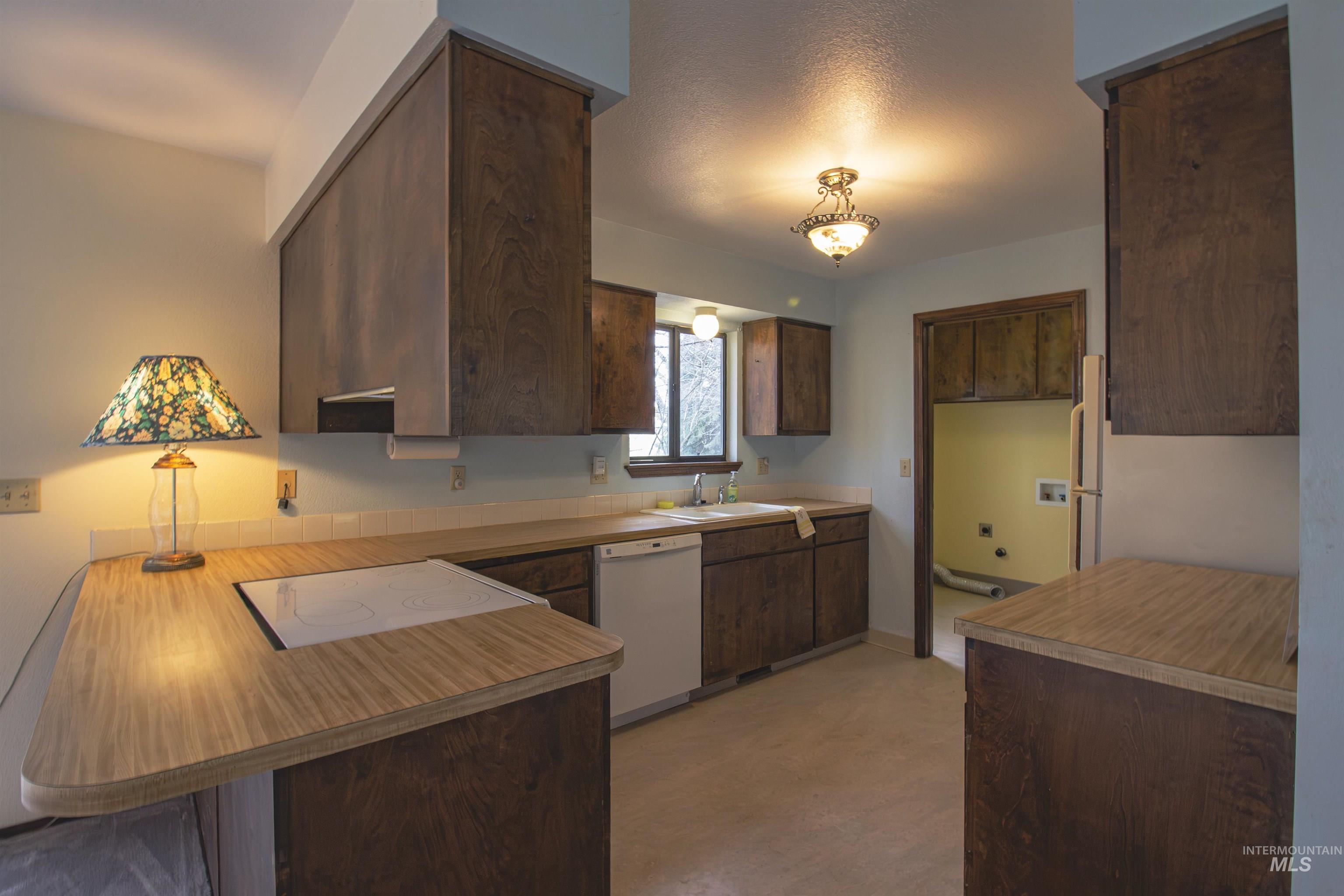 2465 Center Avenue Payette, ID 83661 - Photo 10 of 39 Kitchen featuring dark wood finish cabinetry, white appliances, a peninsula with a breakfast bar, and light countertops