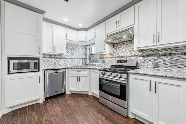 a kitchen with stainless steel appliances granite countertop a stove a sink and white cabinets