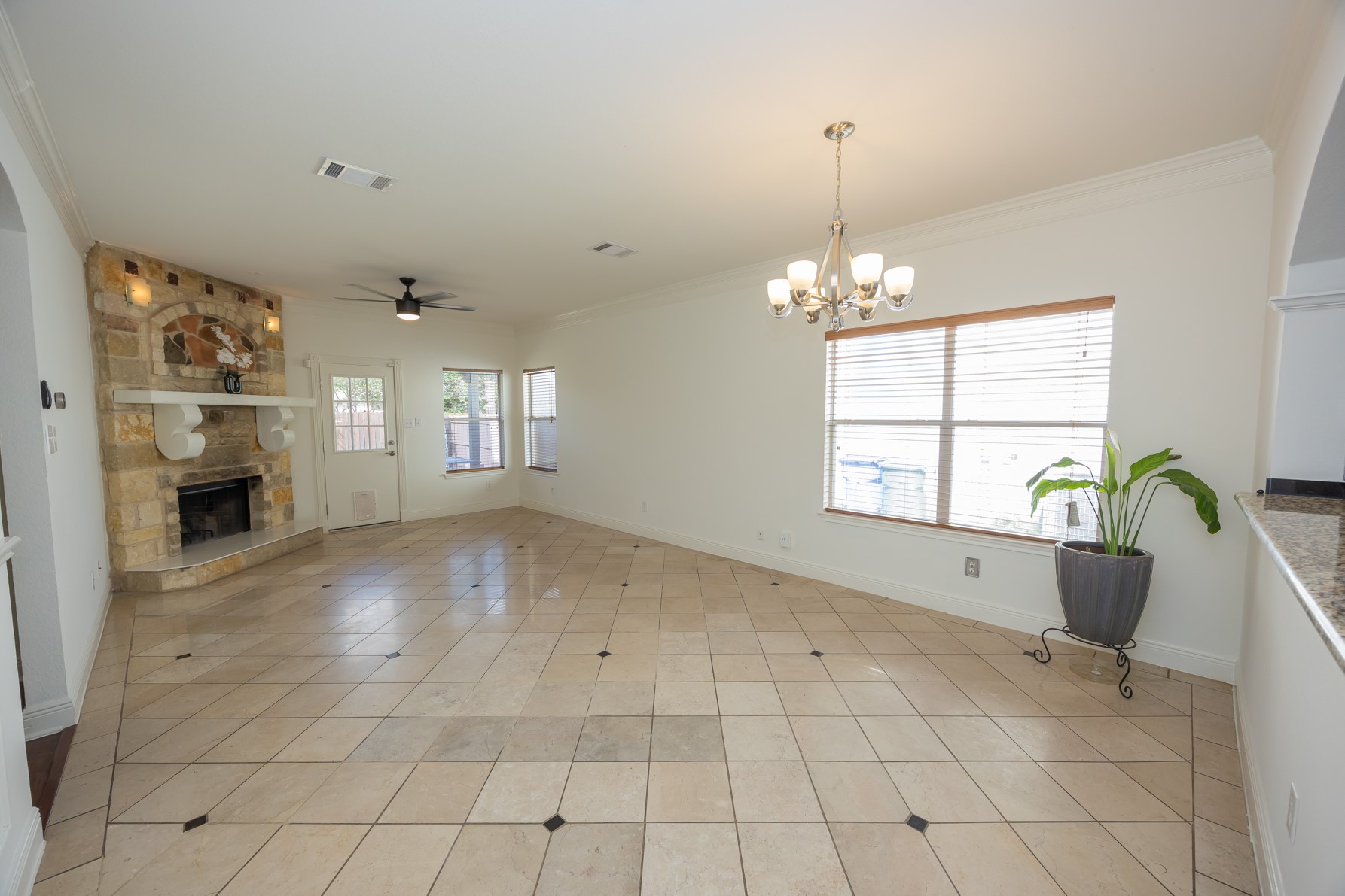 11500 Dimmit Street Manor, TX 78653 - Photo 6 of 14 Spacious living area featuring diagonal tile flooring with accent inserts, a stone-clad fireplace with a decorative mantel, multiple windows with blinds, a ceiling fan, and a chandelier