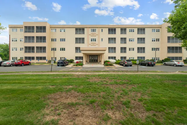 a front view of a building with garden and trees