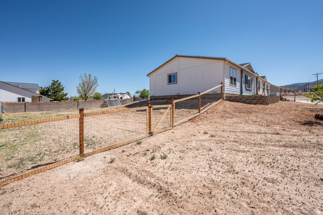 1637 East Midvalley Road Enoch, UT 84721 - Photo 39 of 48 Expansive property featuring a wire-mesh fence with wood posts and gate, a block retaining wall, and a white-sided exterior