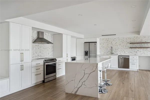 a kitchen with stainless steel appliances granite countertop a stove top oven a sink and white cabinets with wooden floor