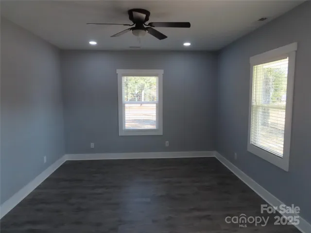 an empty room with wooden floor ceiling fan and windows