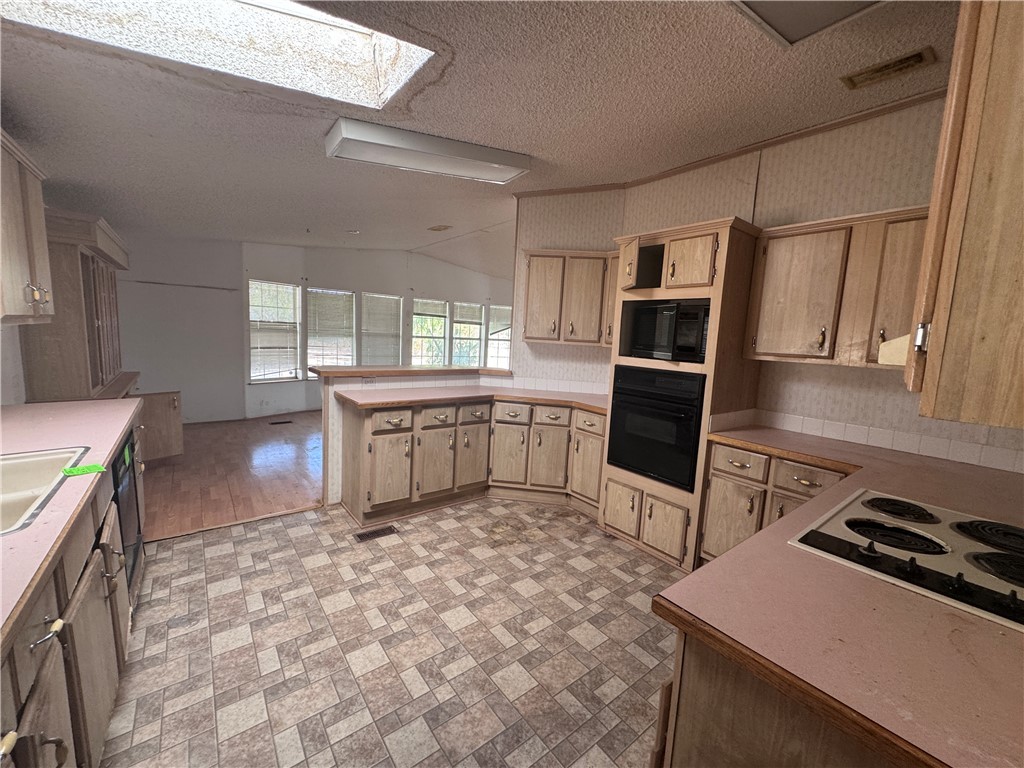 3053 McConnico Road Golden Valley, AZ 86413 - Photo 15 of 18 Kitchen featuring light countertops, black appliances, a textured ceiling, a skylight, and lofted ceiling