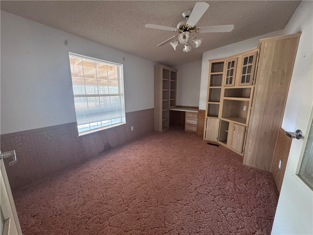 3053 McConnico Road Golden Valley, AZ 86413 - Photo 4 of 18 Unfurnished living room with dark carpet, a wainscoted wall, wood walls, a textured ceiling, and a ceiling fan