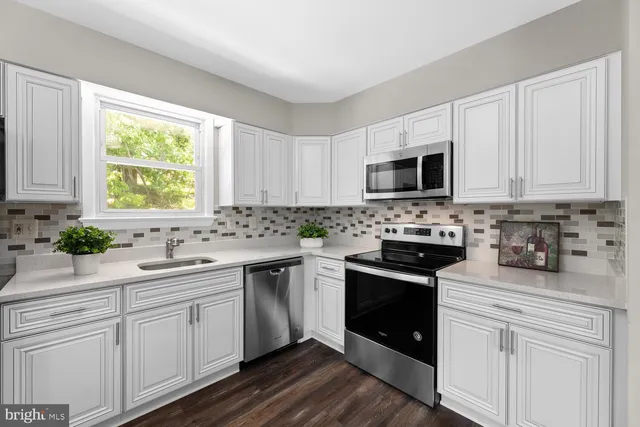 a kitchen with white cabinets appliances a sink and a window