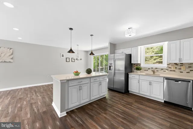 a kitchen with stainless steel appliances granite countertop a refrigerator a sink dishwasher a stove and white countertops with wooden floor