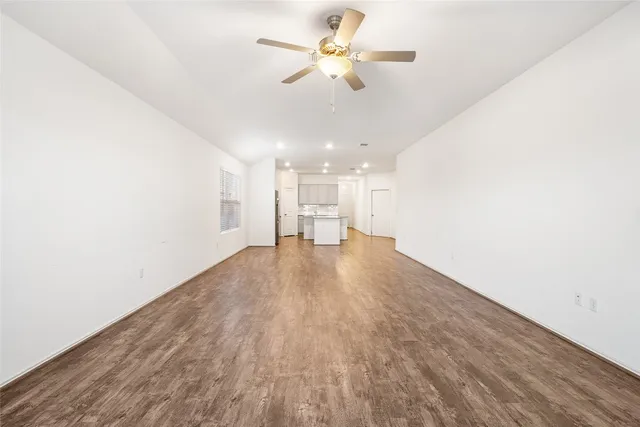 an empty room with wooden floor chandelier fan and windows