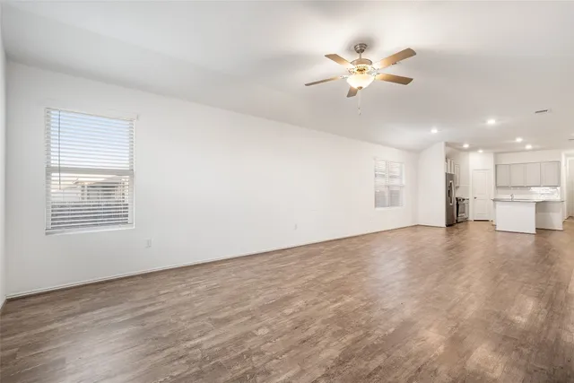 an empty room with wooden floor ceiling fan and windows