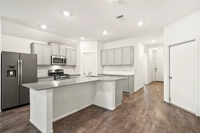 a kitchen with stainless steel appliances a stove top oven a sink a refrigerator white cabinets and wooden floor