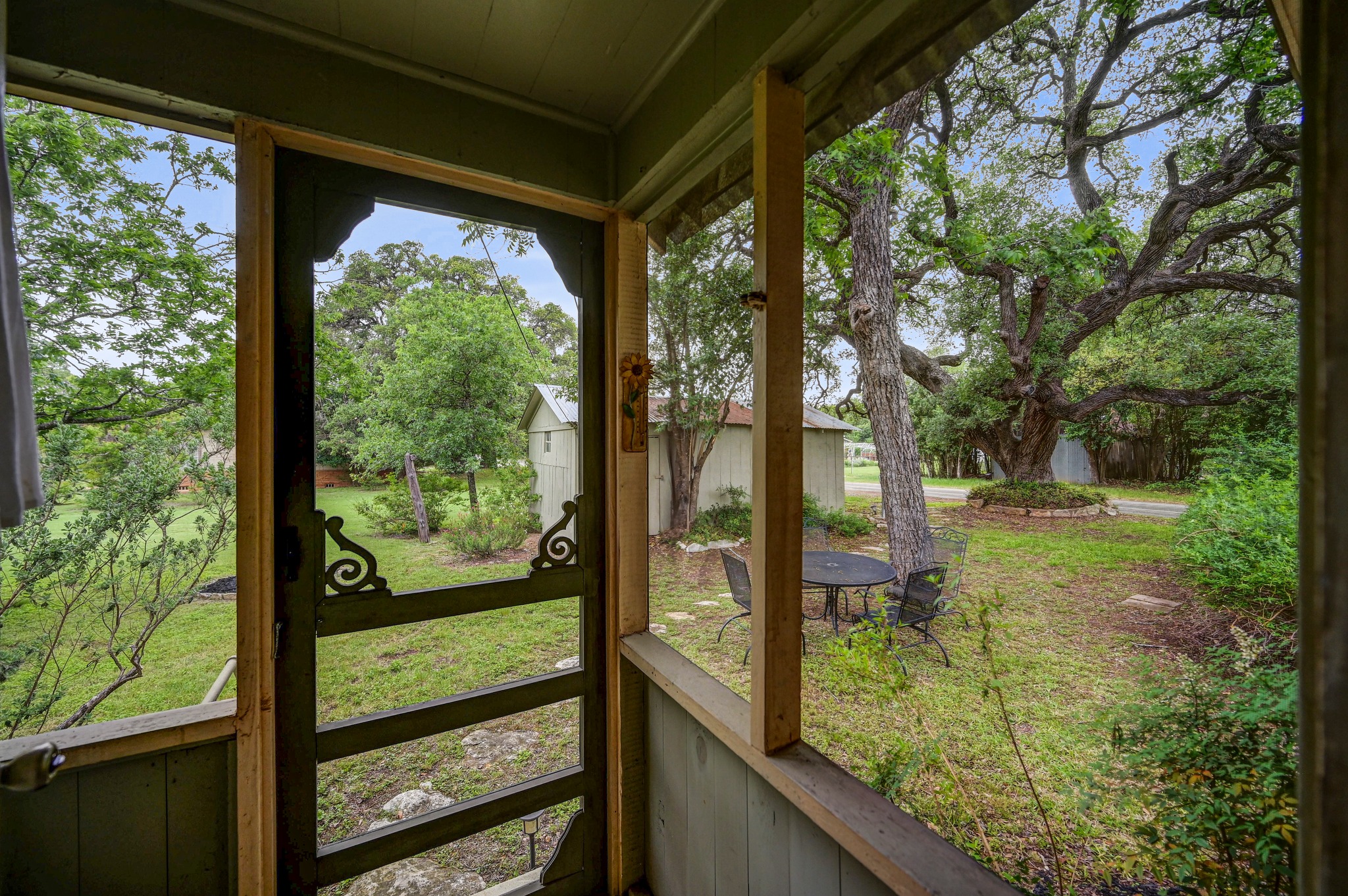 719 Elm Street Blanco, TX 78606 - Photo 20 of 25 Expansive outdoor space featuring a decorative screen door, lush green landscaping, mature trees, and an accessory building