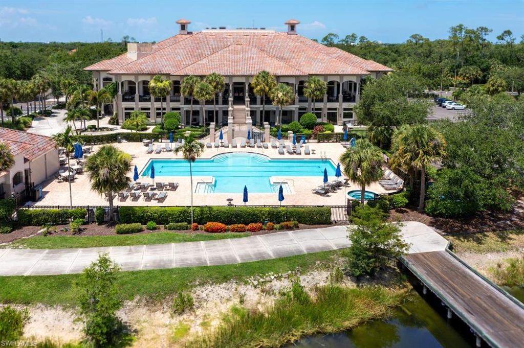 20117 Seadale Court Estero, FL 33928 - Photo 29 of 34 Large-scale clubhouse with terracotta roof tiles, expansive swimming pool, integrated hot tub, surrounding paved deck, and adjacent water feature with a wooden bridge