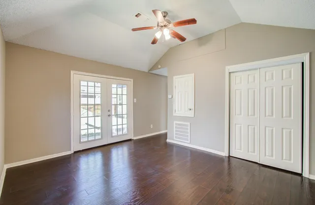an empty room with wooden floor chandelier fan and windows