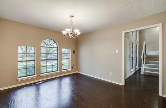 an empty room with wooden floor chandelier and windows