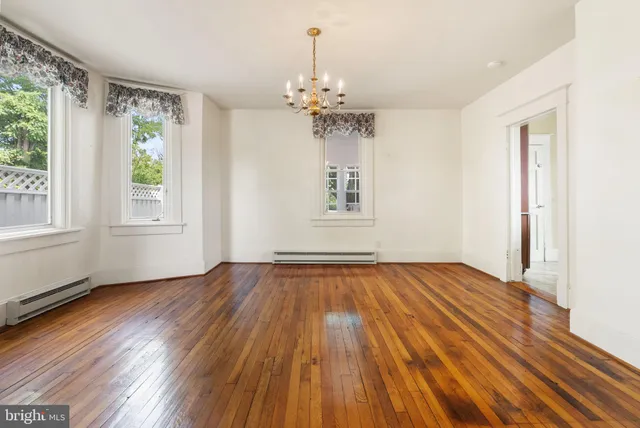 an empty room with wooden floor chandelier and windows