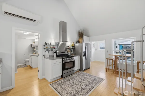 a kitchen with stainless steel appliances kitchen island granite countertop a refrigerator a stove and white cabinets with wooden floor