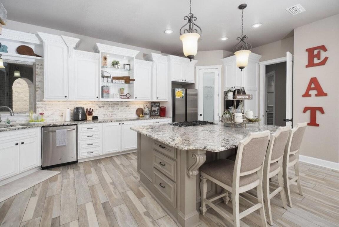 8 West Lakeshore Drive Ransom Canyon, TX 79366 - Photo 14 of 44 a kitchen with stainless steel appliances kitchen island granite countertop a wooden floor and white cabinets