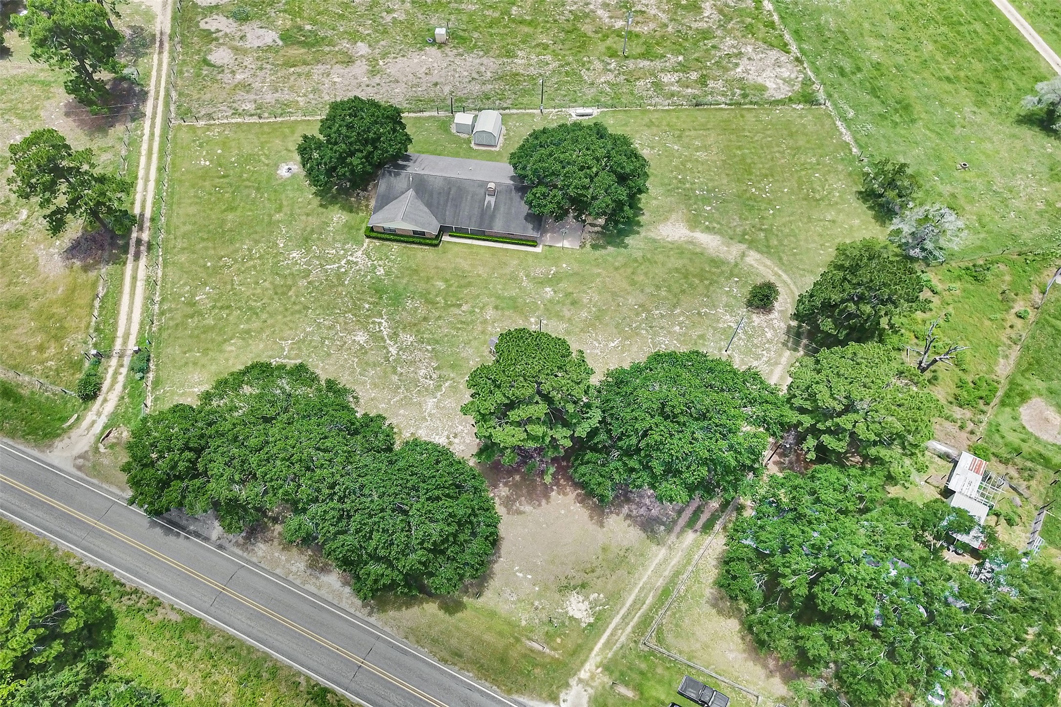 341 South S Loop Bellville, TX 77418 - Photo 2 of 33 This aerial view showcases a spacious property with a single-story house surrounded by lush greenery and mature trees. It features a large, open yard, a long driveway, and is bordered by a quiet road, offering privacy and a rural feel.