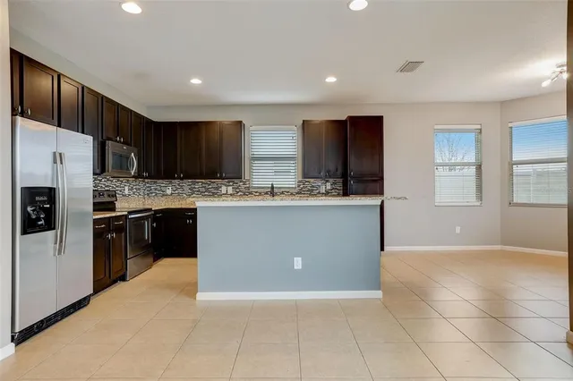 a large kitchen with stainless steel appliances kitchen island granite countertop a refrigerator a stove a sink and a oven