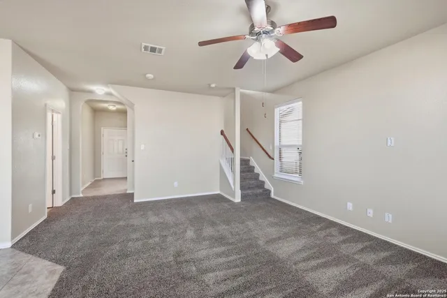 an empty room with chandelier fan and windows
