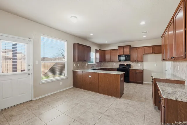 a large kitchen with stainless steel appliances granite countertop a stove a sink dishwasher a refrigerator and white cabinets with wooden floor