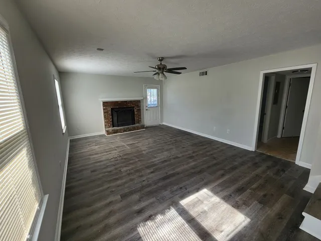 an empty room with wooden floor fireplace and windows