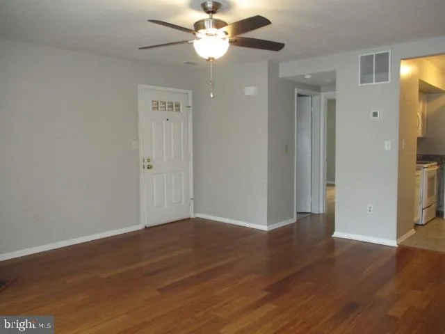 a view of an empty room with wooden floor and a ceiling fan