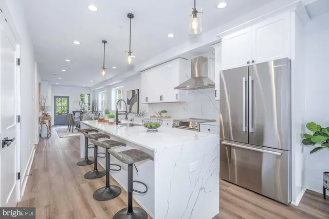 a kitchen with stainless steel appliances granite countertop a refrigerator a sink dishwasher a stove a dining table and chairs with wooden floor