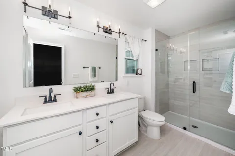 a bathroom with a double vanity sink toilet mirror and shower