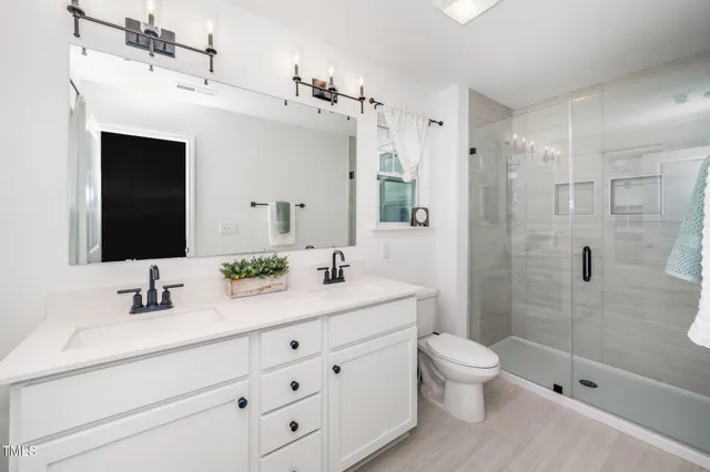 a bathroom with a double vanity sink toilet mirror and shower