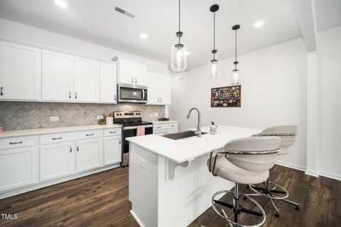 a kitchen with stainless steel appliances granite countertop a sink a stove a refrigerator and white cabinets with wooden floor