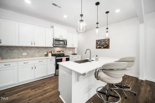 a kitchen with stainless steel appliances granite countertop a sink a stove a refrigerator and white cabinets with wooden floor