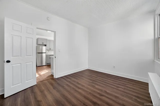 a view of empty room with wooden floor and kitchen