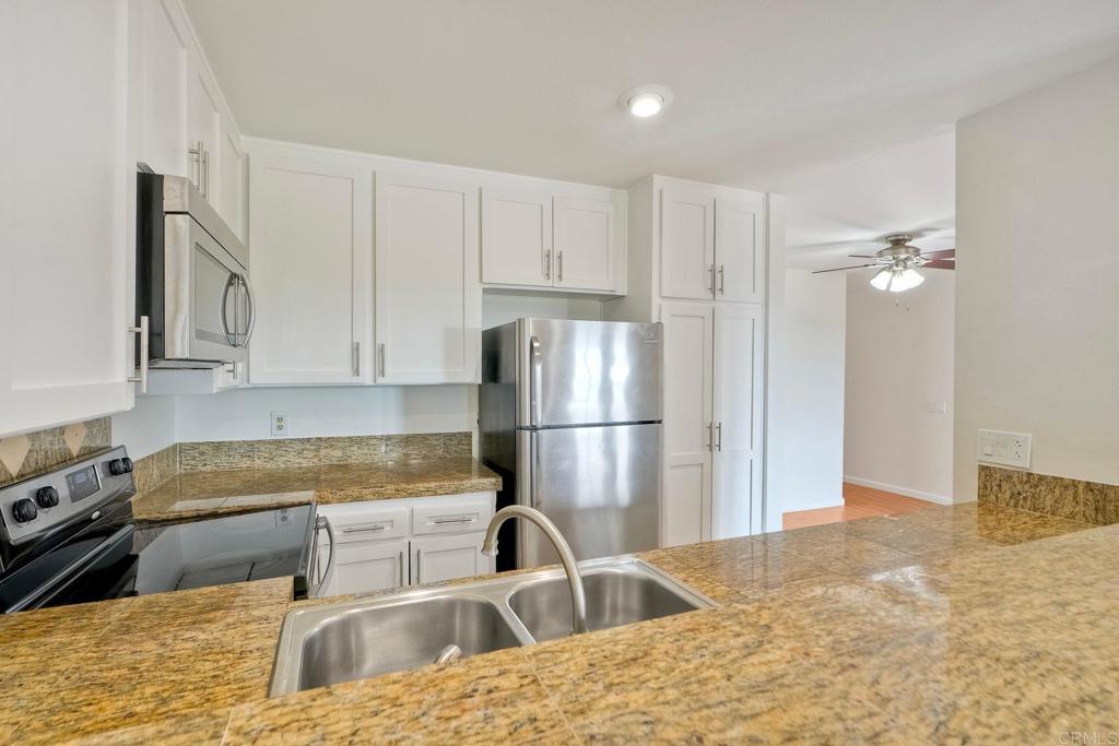 2251 Altisma Way, Unit 202 Carlsbad, CA 92009 - Photo 24 of 35 a kitchen with stainless steel appliances granite countertop a refrigerator a sink a stove with white cabinets