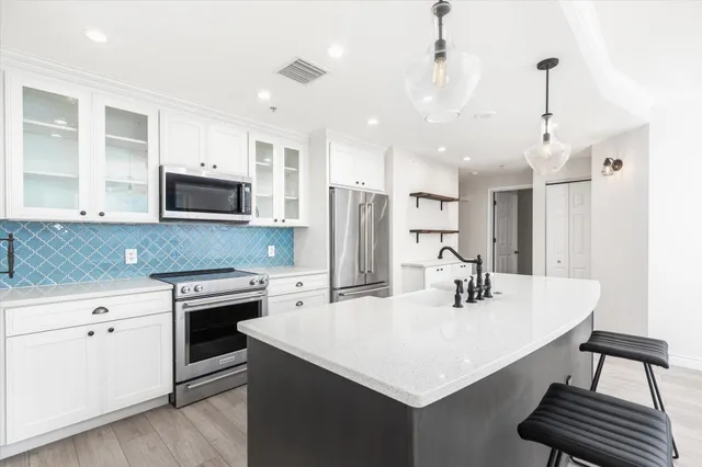 a kitchen with stainless steel appliances a sink a stove a refrigerator a center island and cabinets