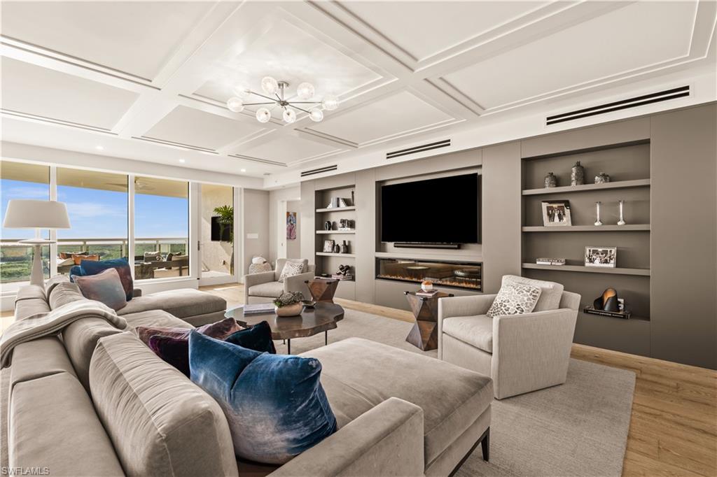 Living area with built in features, coffered ceiling, a chandelier, and wood finished floors